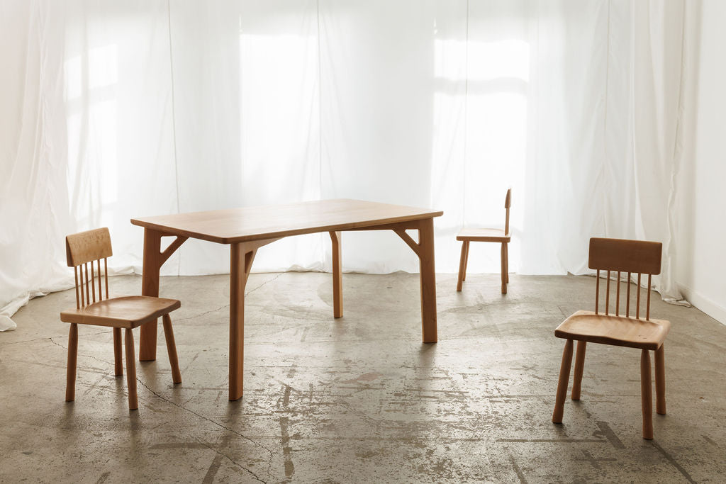  A simple wooden table with three chairs placed in an empty room, creating a minimalistic and inviting atmosphere.